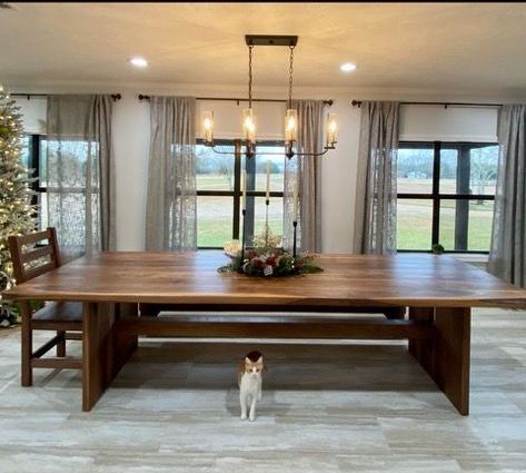 A cat is standing under a wooden table in a dining room