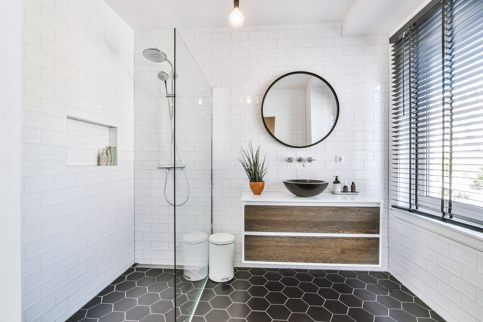 A bathroom with a walk in shower , sink , mirror and window.