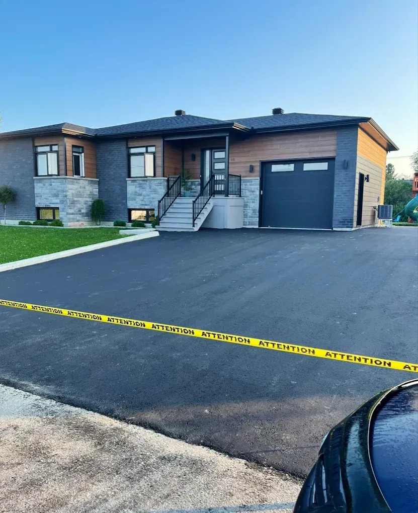Maison moderne de plain-pied avec une grande allée noire, un garage et un ruban de signalisation jaune au premier plan.