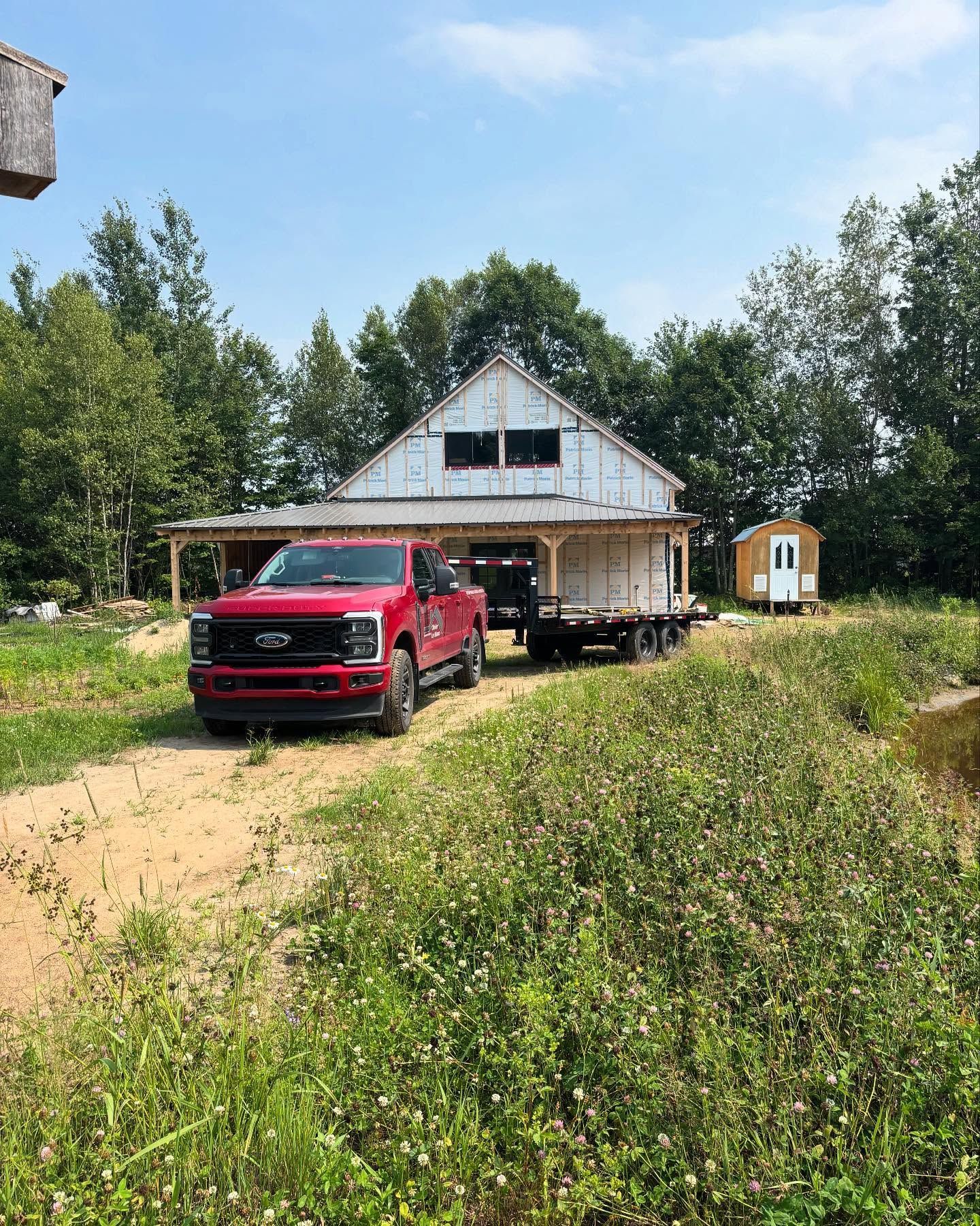 Une camionnette rouge est garée devant une maison rustique avec une véranda, entourée d'herbe et d'arbres.