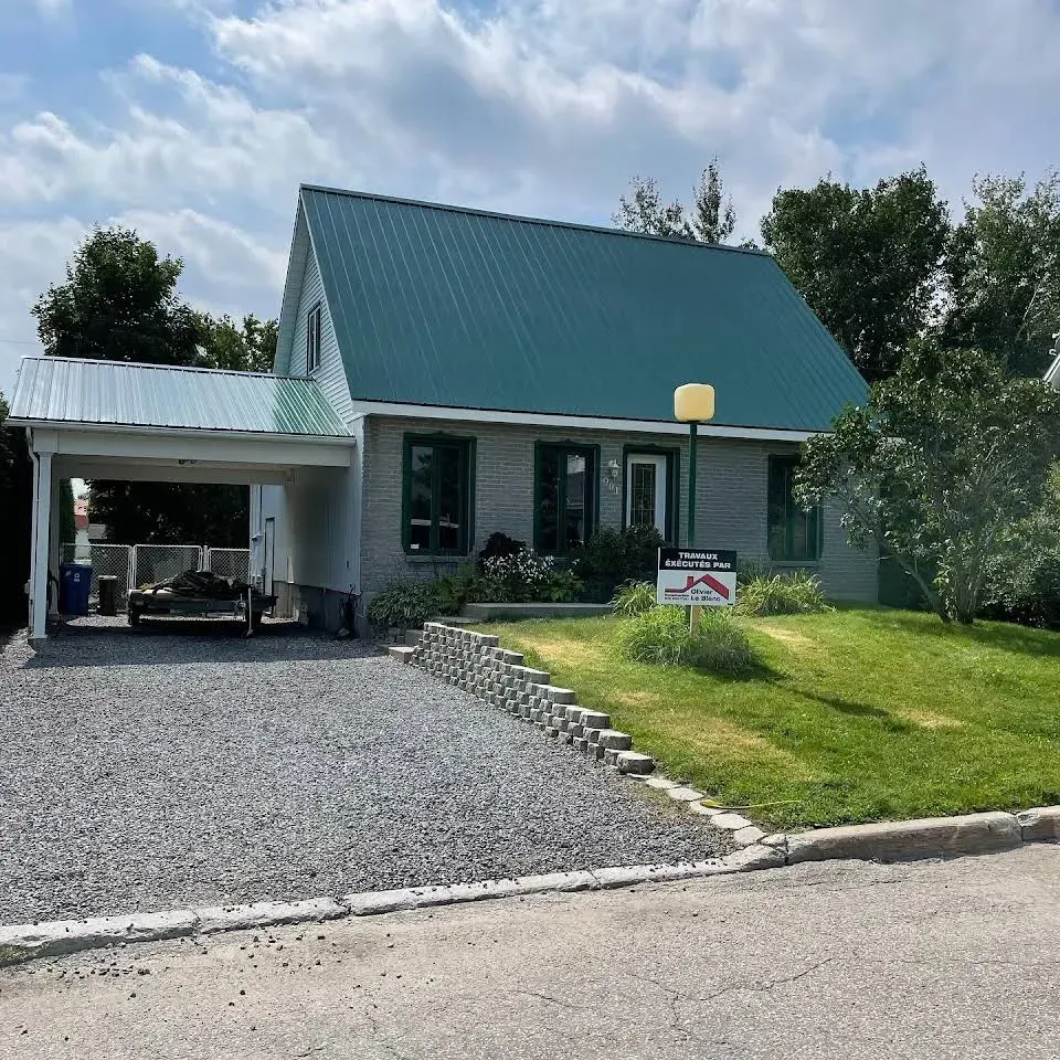 Petite maison avec toit turquoise, abri voiture, allée gravillonnée et jardin gazonné à l'avant, située dans une rue calme.