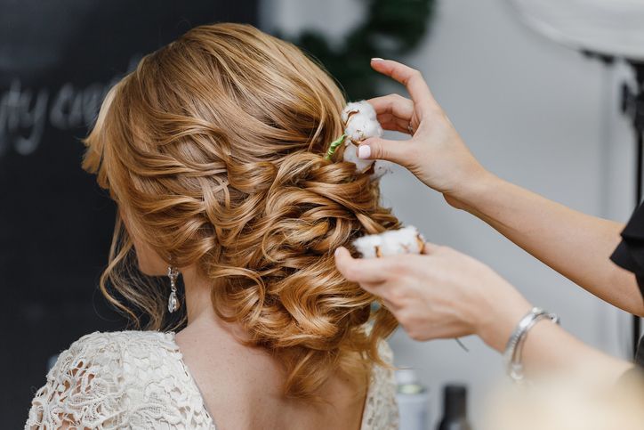 Hair stylist or florist makes the bride a wedding hairstyle with fresh cotton flowers