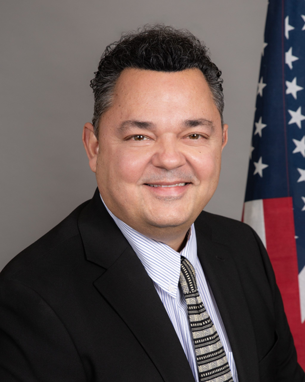 Portrait of a smiling man in a suit beside an American flag
