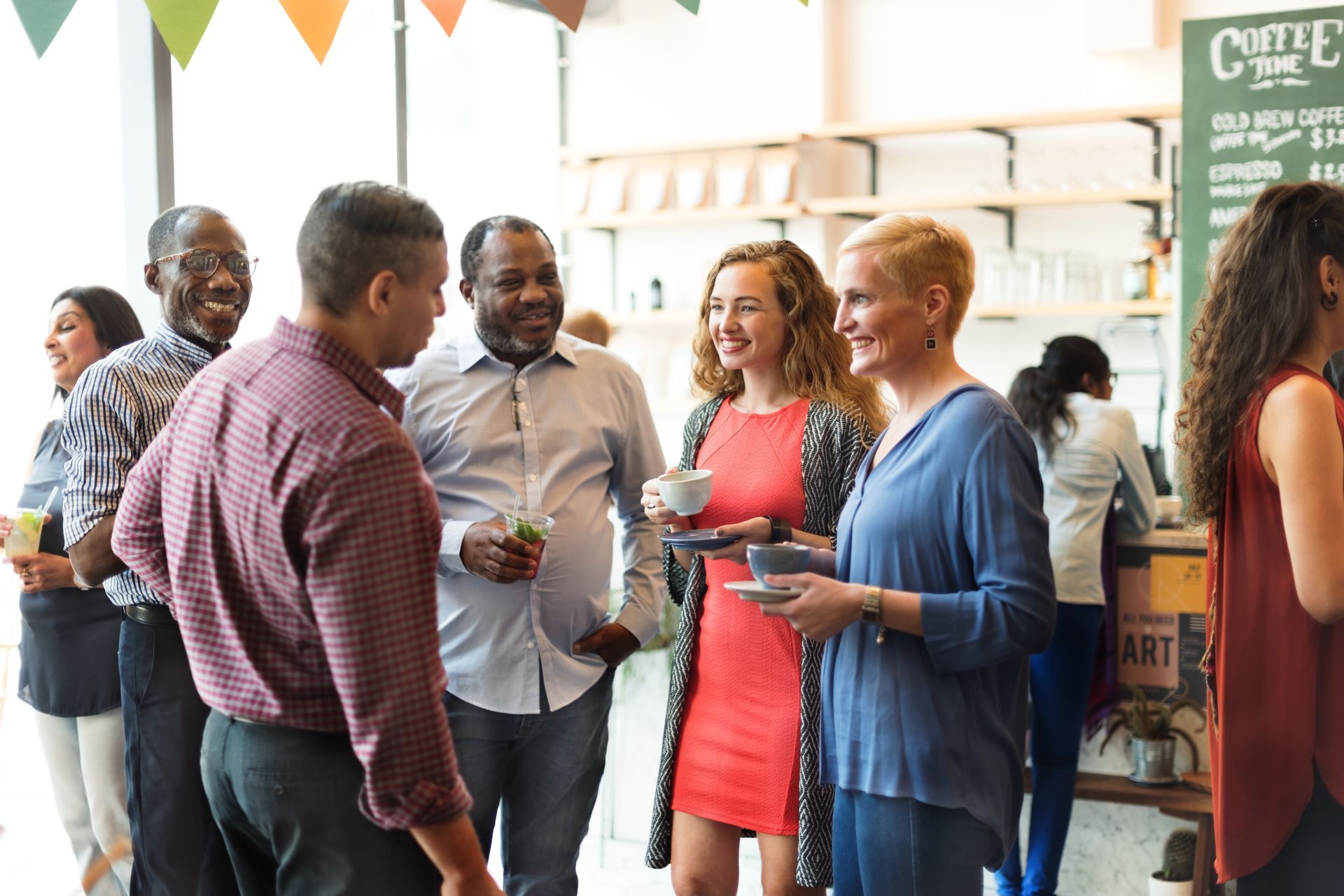 People chatting and holding drinks at a lively indoor social gathering with colorful bunting.