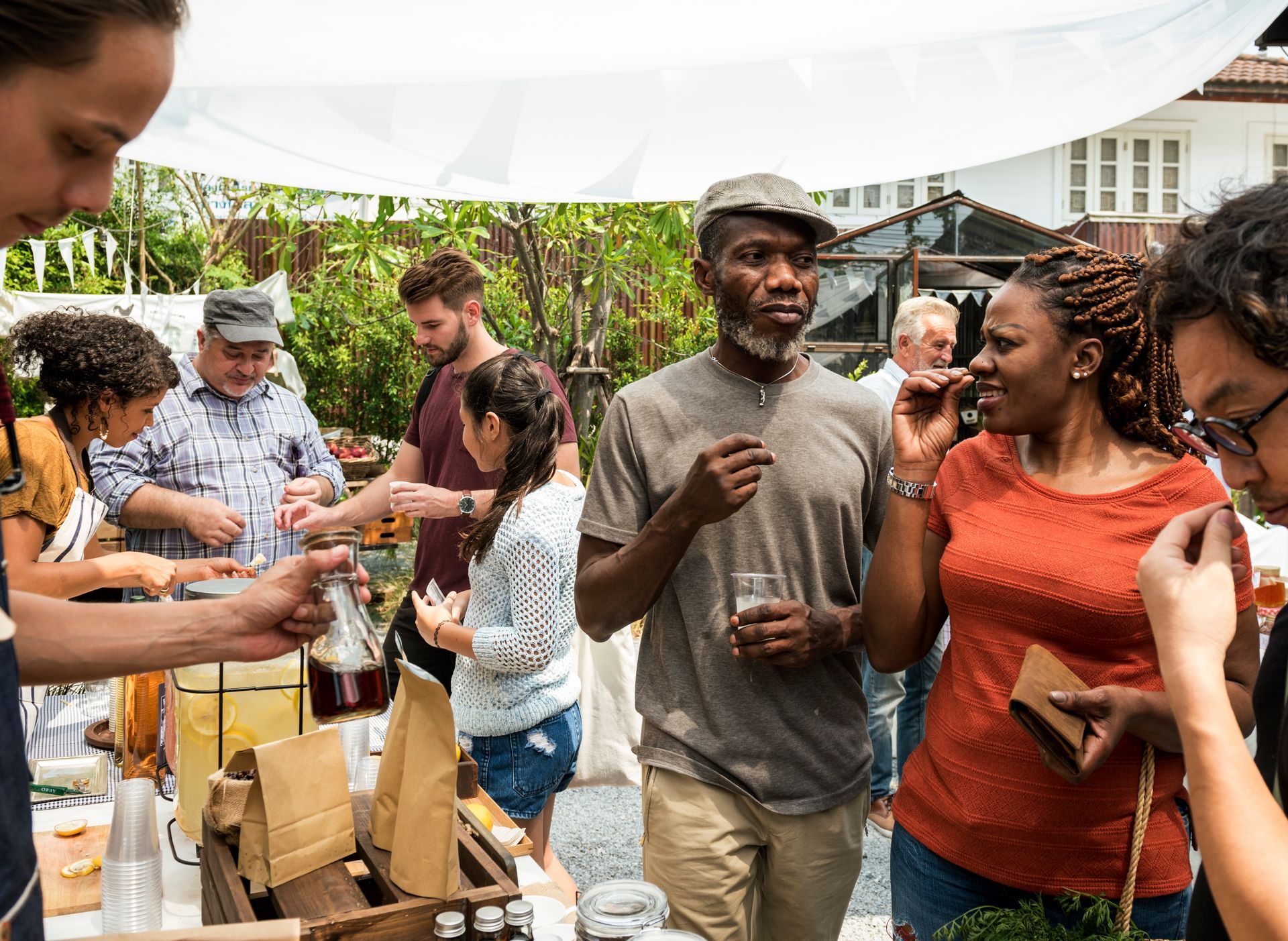 People browsing and serving food at an outdoor community event under a white canopy.