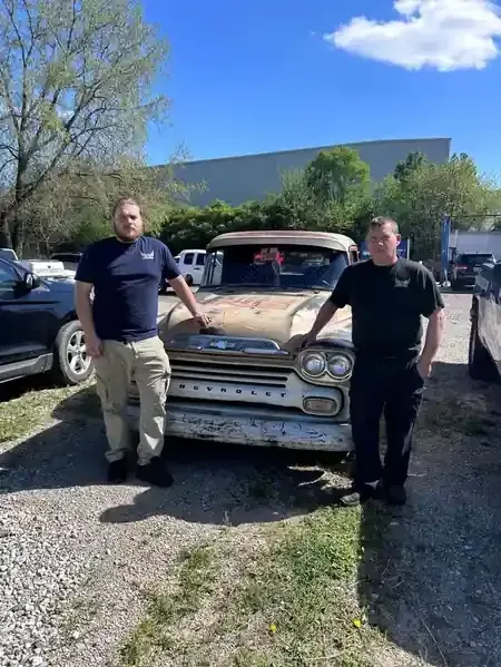 Two people standing beside an old truck in a sunny parking lot