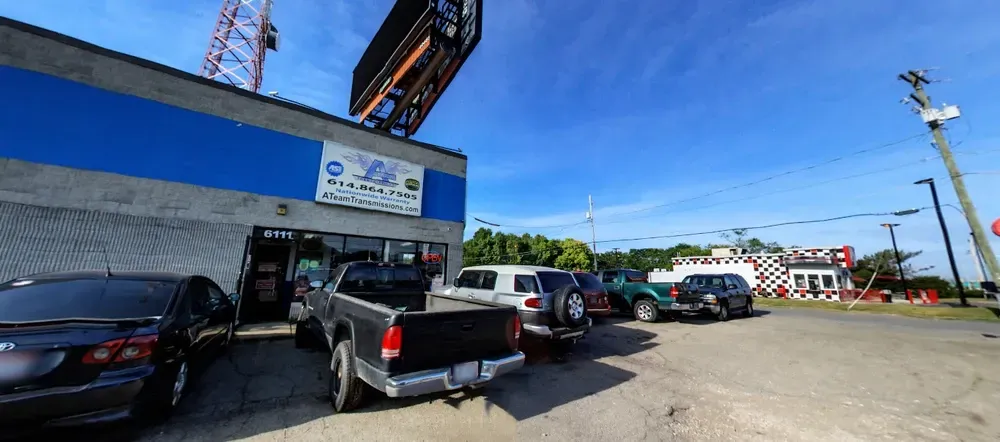 Street view of a blue storefront with parked cars and a pickup truck under a bright sky.