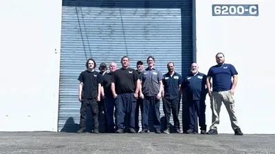 Eight people standing outside a warehouse door with the number 6200-C above it