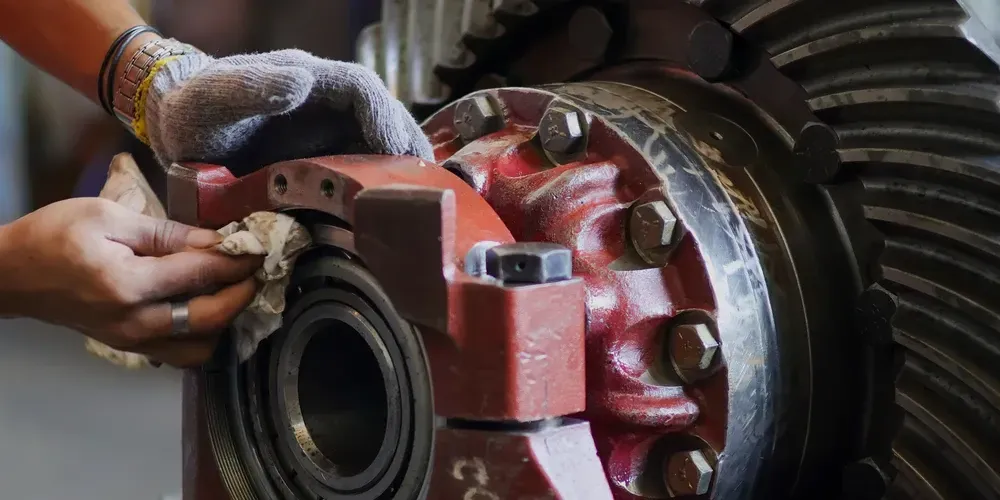 Hands in gloves working on a red industrial machine bearing with a wrench