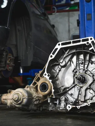 Detached car transmission and drivetrain parts on a garage floor, with a blue lift in the background