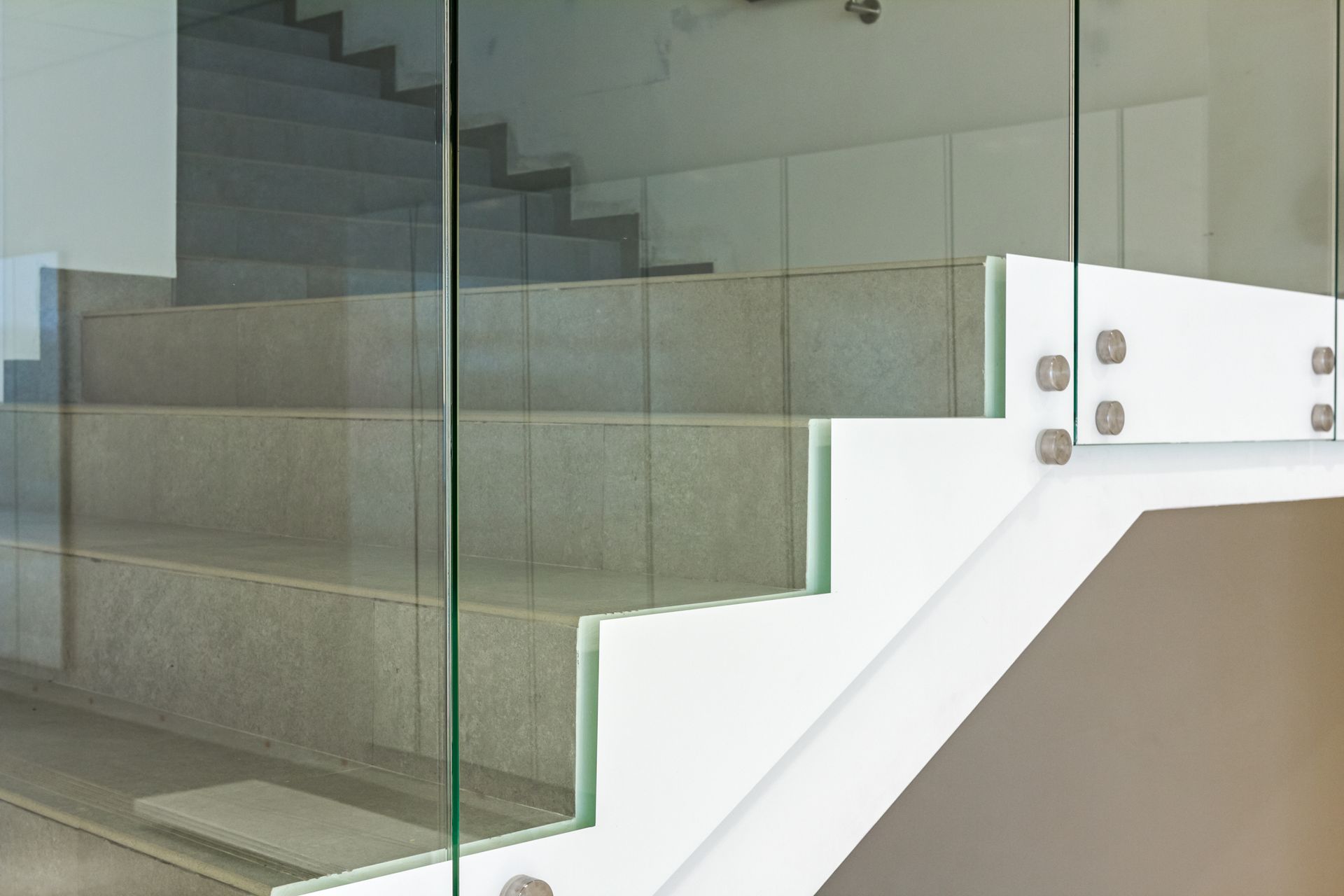 Un escalier moderne avec des marches en pierre et une rambarde en verre fixée par des entretoises latérales en métal argenté.