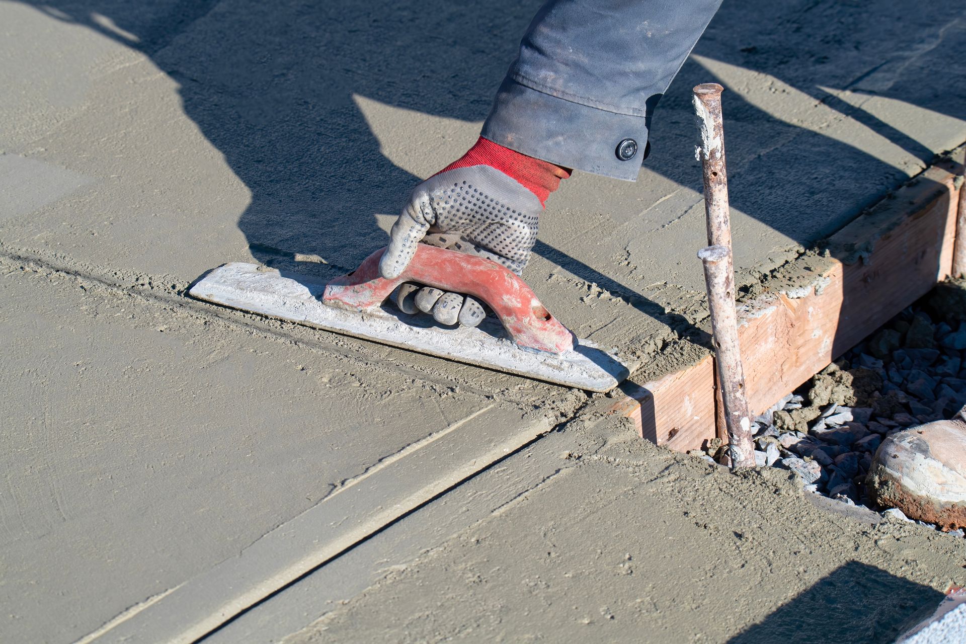 Une main gantée utilise une truelle métallique pour lisser le béton humide le long du bord d'un coffrage en bois.