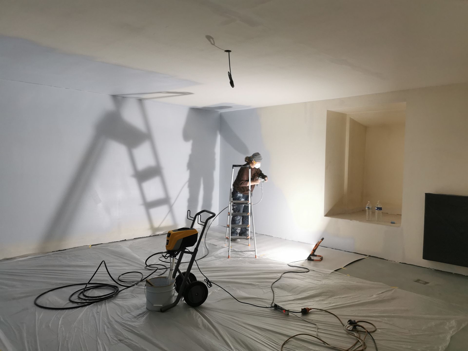 A man is standing on a ladder in a room with a shadow on the wall.