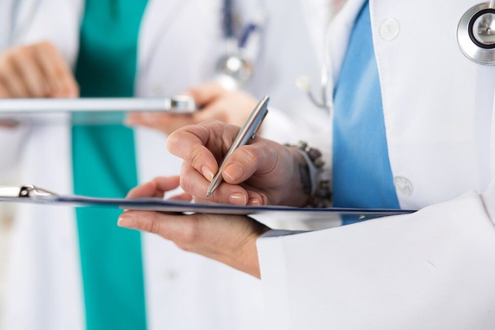 A Doctor Is Writing On A Clipboard With A Pen — Health Hub Mackay In Airlie Beach, QLD
