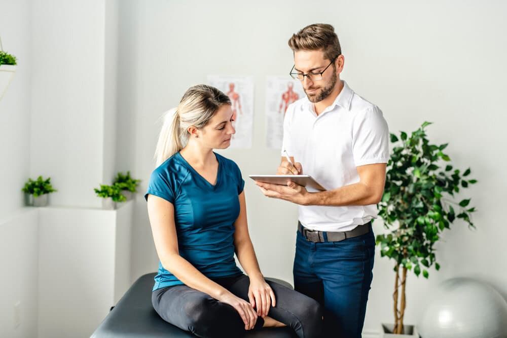 A Man Is Talking To A Woman Who Is Sitting On A Table — Health Hub Mackay In Proserpine, QLD