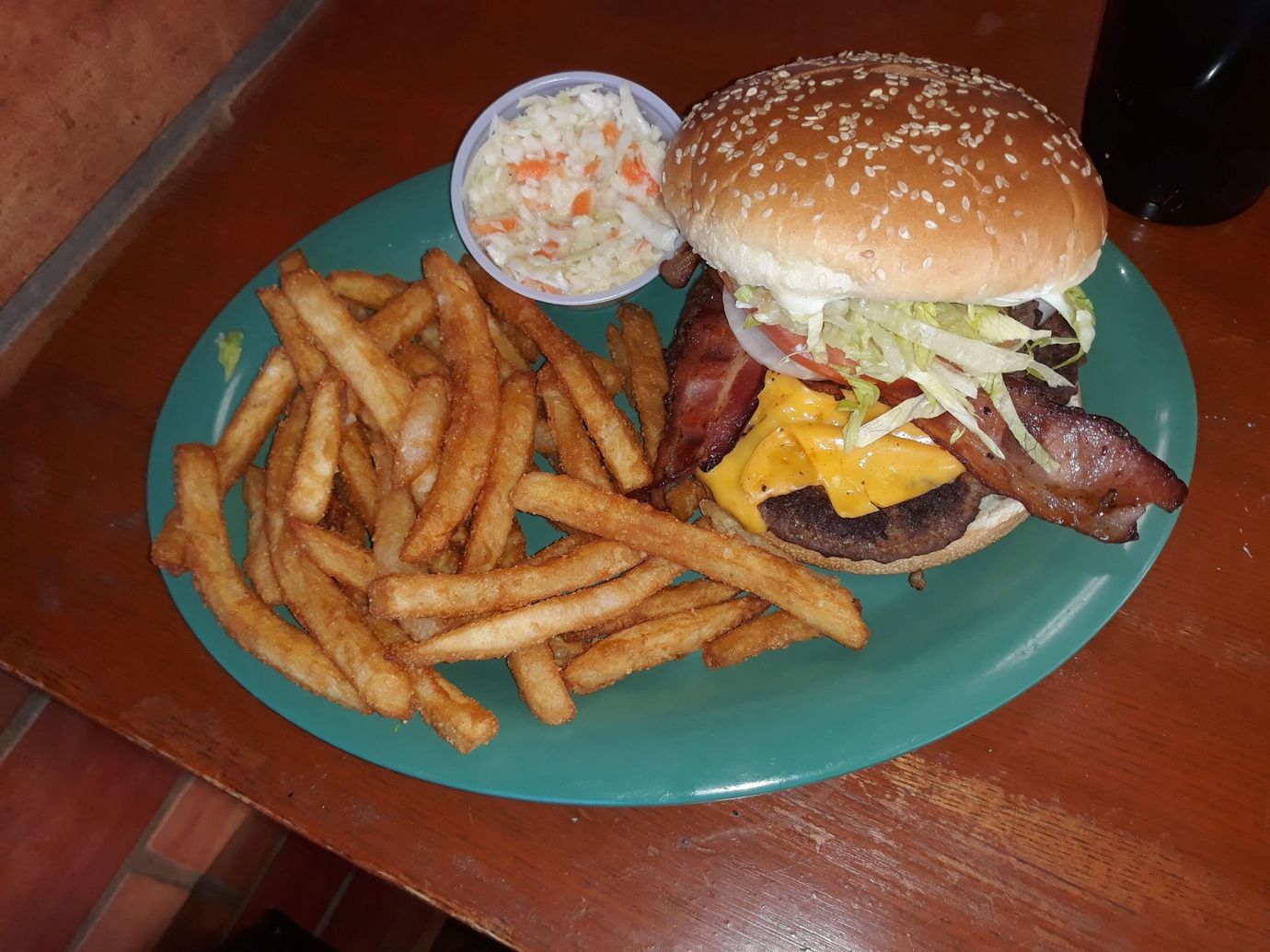 Burger with bacon, fries, and coleslaw on a green plate on a wooden table