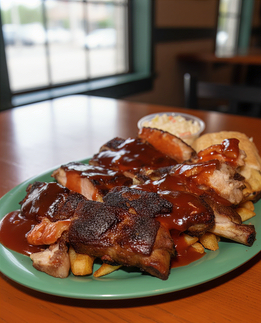 Plate of ribs and fries topped with barbecue sauce on a green plate at a restaurant table