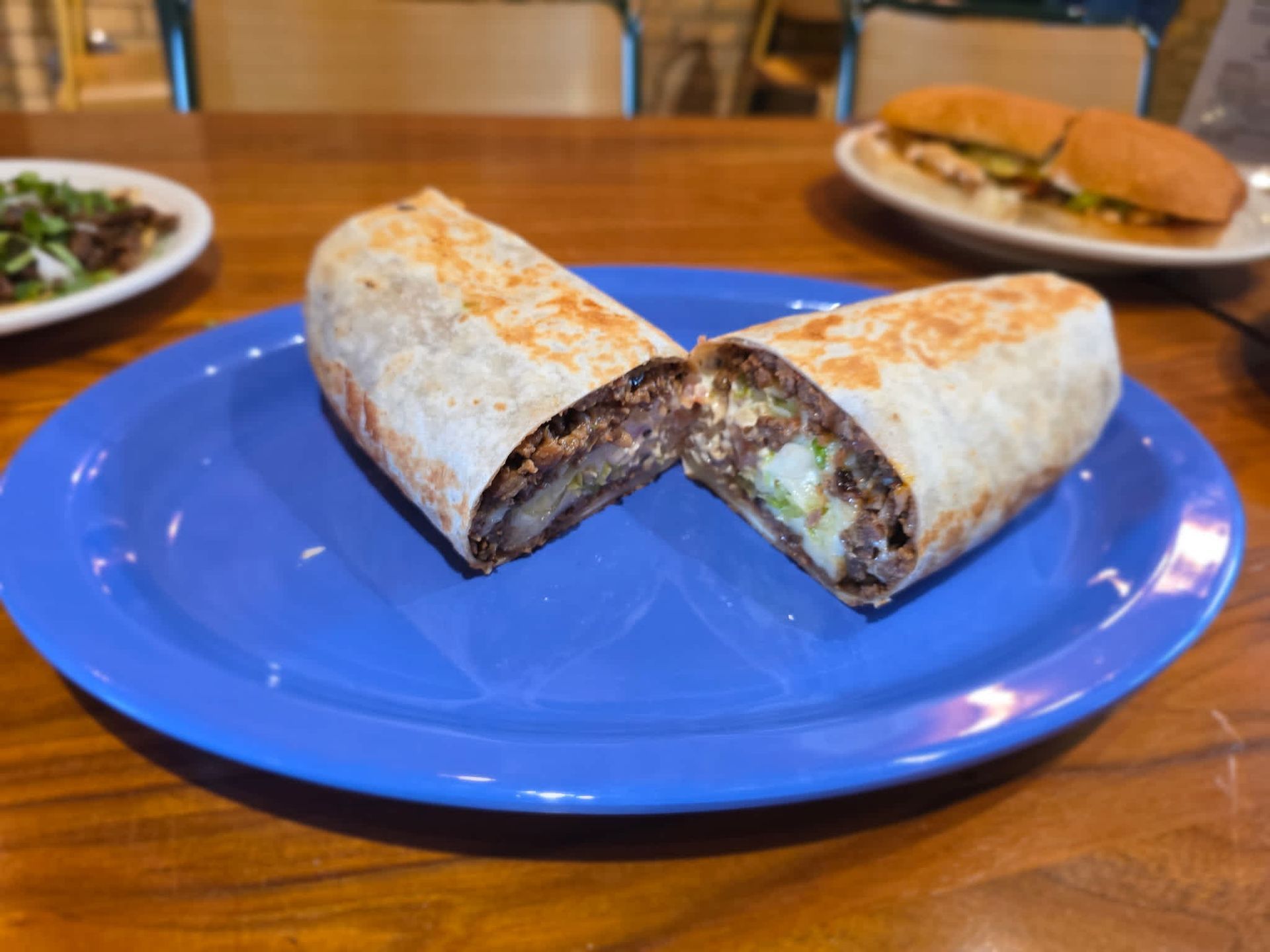 Cut burrito on a blue plate with another plate of food in the background