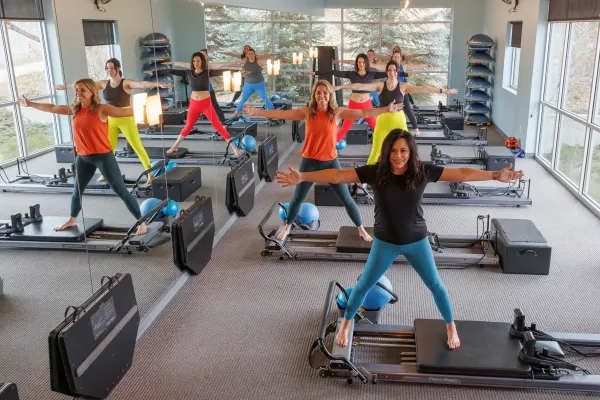 Pilates class in a bright studio, people exercising on reformer machines in colorful workout clothes