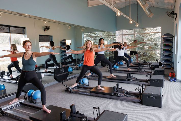 Women doing Pilates on reformers in a bright studio, arms extended during a workout class
