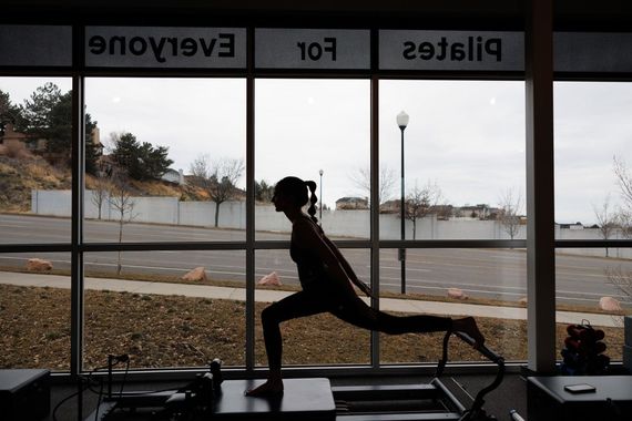 Silhouette of a person stretching in a gym by large windows, with “Pilates for Everyone” signage above.