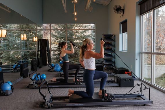 Two people exercising on Pilates reformers in a bright studio with mirrors and exercise balls