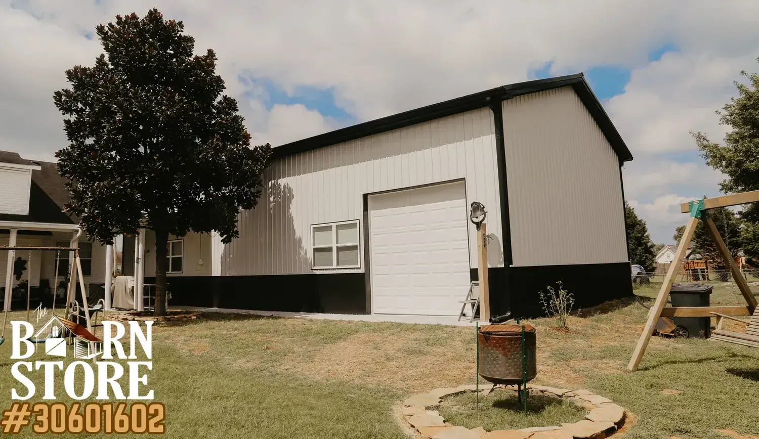 A modern barn house with a white and black exterior, featuring a large garage door and surrounded by a green yard with a tree and playground equipment.