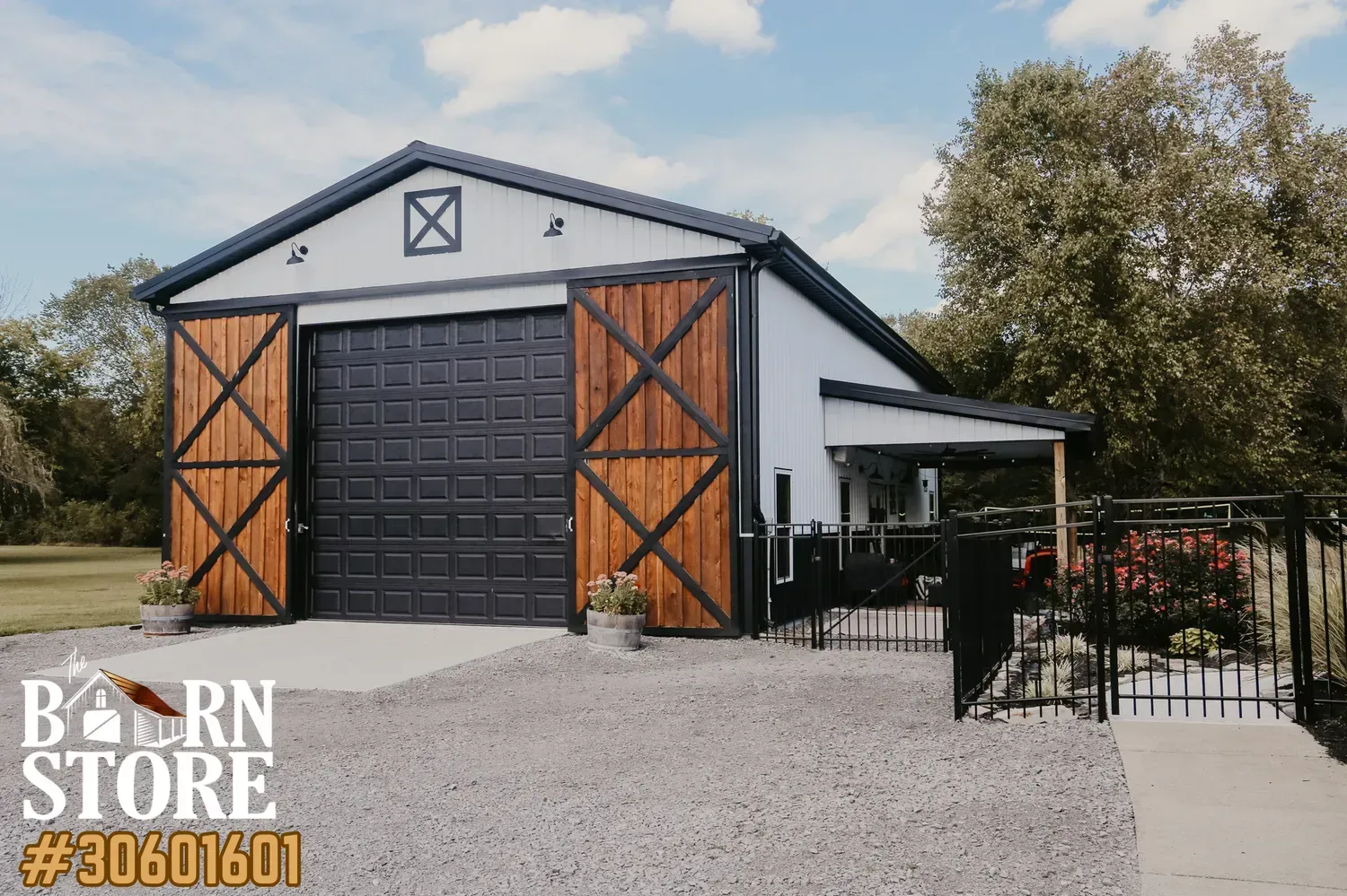 Modern barn builders near you feature with a black garage door and wooden accents, surrounded by a gravel driveway and a fenced garden area.
