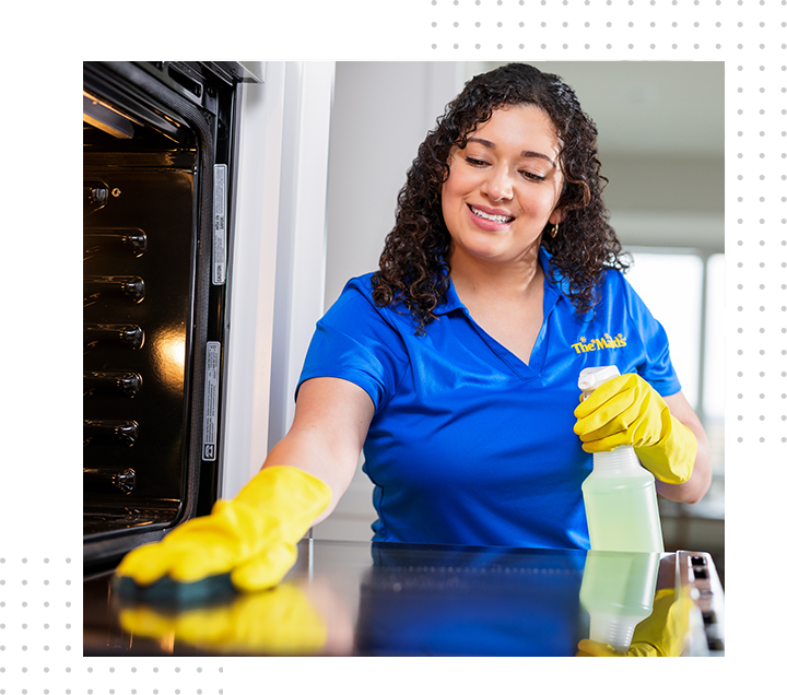 Woman in blue shirt and yellow gloves cleaning an oven with a spray bottle