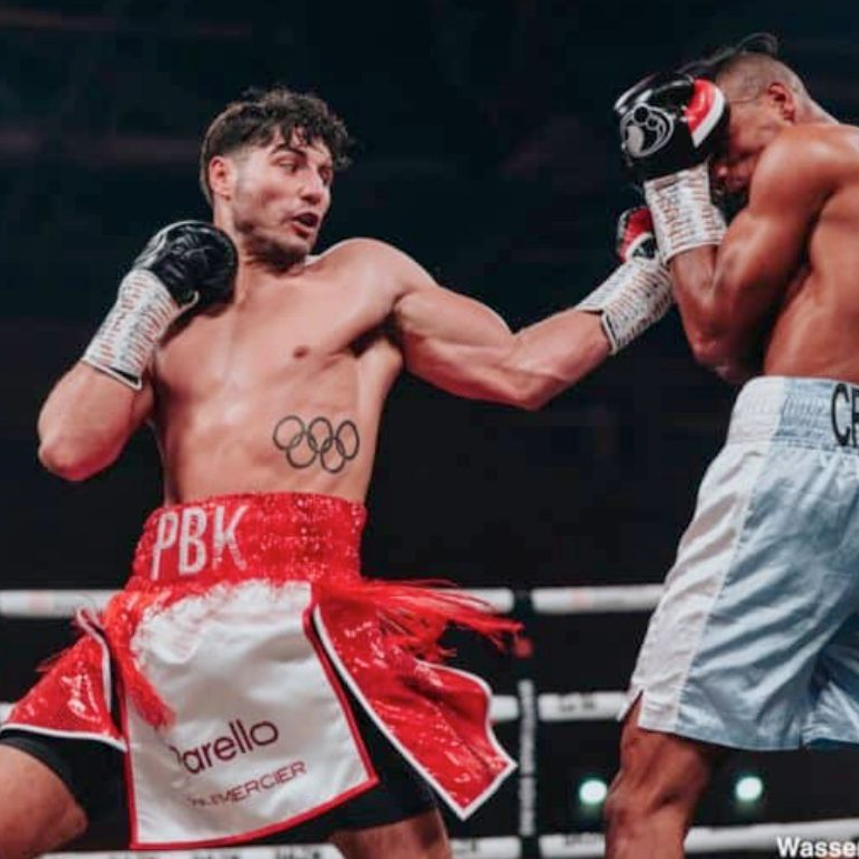 Boxer throwing a punch in a boxing ring, red and white shorts with Olympic rings on display.