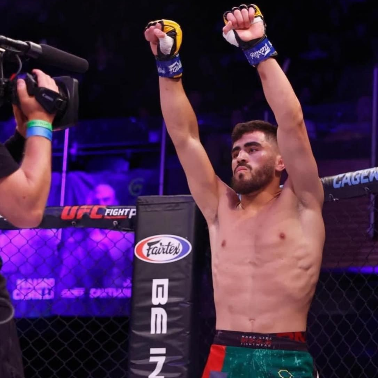 MMA fighter raising arms in victory, wearing green shorts, with a stadium background.