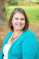 Amber Strangs, a woman smiles, wearing turquoise cardigan, turquoise earrings, necklace, white top, outdoors.