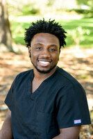 Smiling person in black scrubs outdoors.