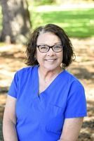 Ladonna Trautz, a woman with glasses smiles in blue scrub top outdoors.
