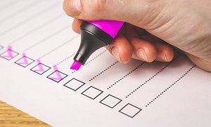 Hand with a pink highlighter marking check boxes on a list.