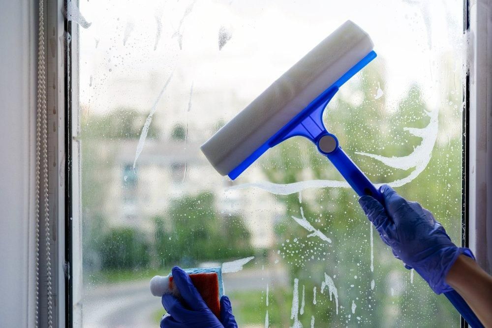 A Person Is Cleaning a Window with A Squeegee — KJ's Elite Cleaning Services Newcastle in East Maitland, NSW