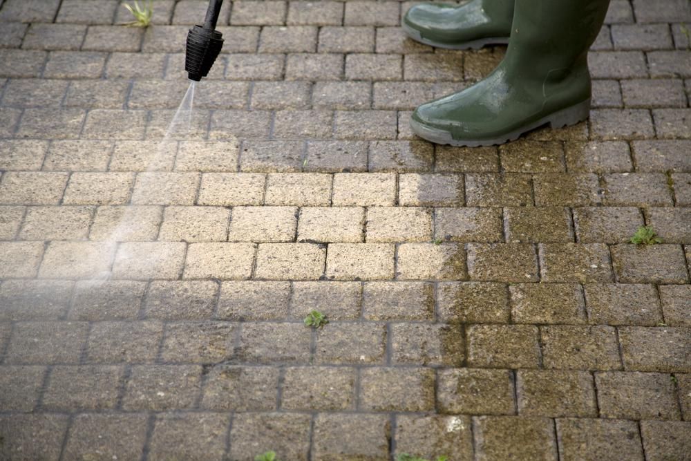 Person in green boots pressure-washing a brick sidewalk at a close angle