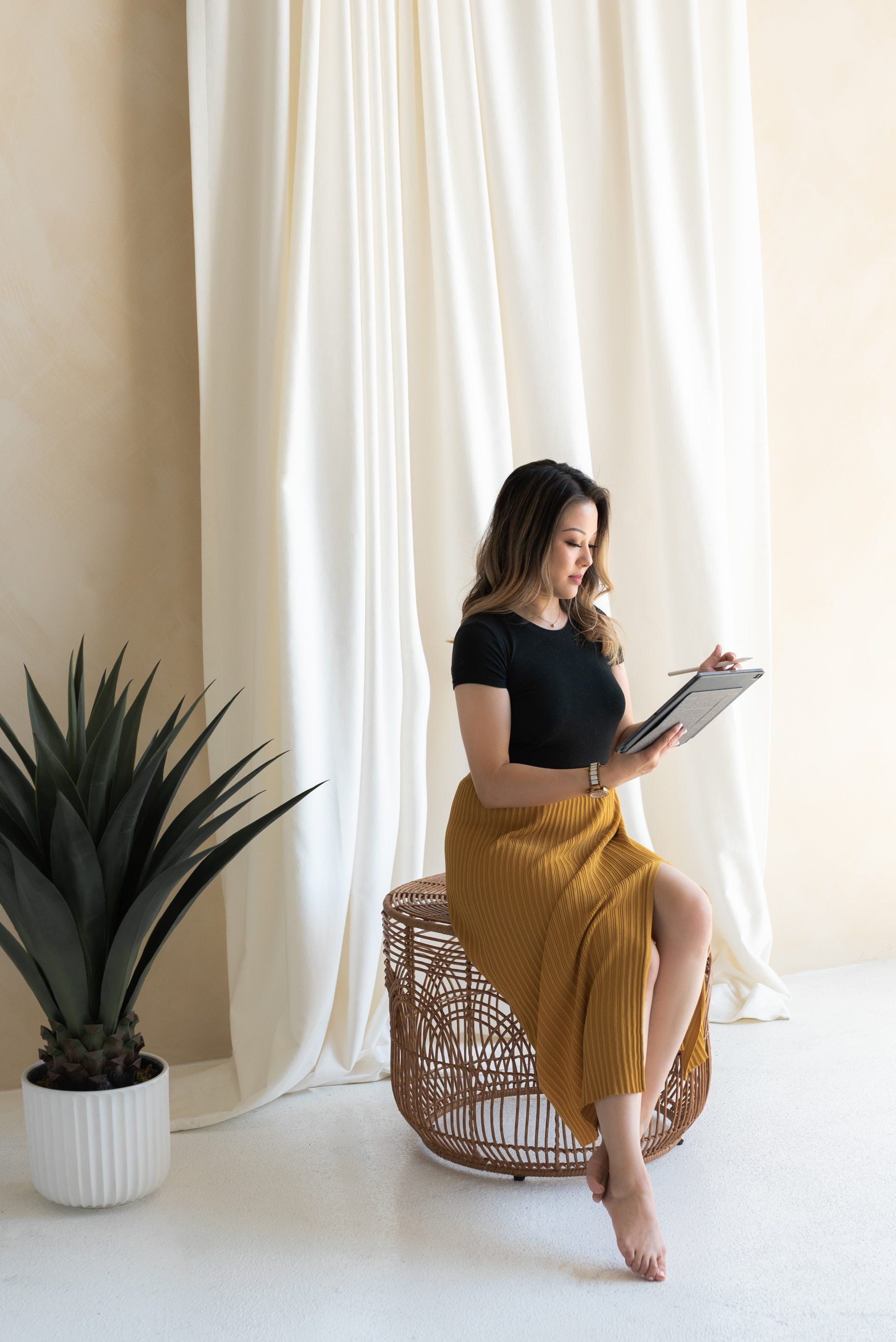 Female spa owner reads from a tablet while sitting on a large wicker ottoman spa owner, reads from tablet while sitting on large wicker cassinet