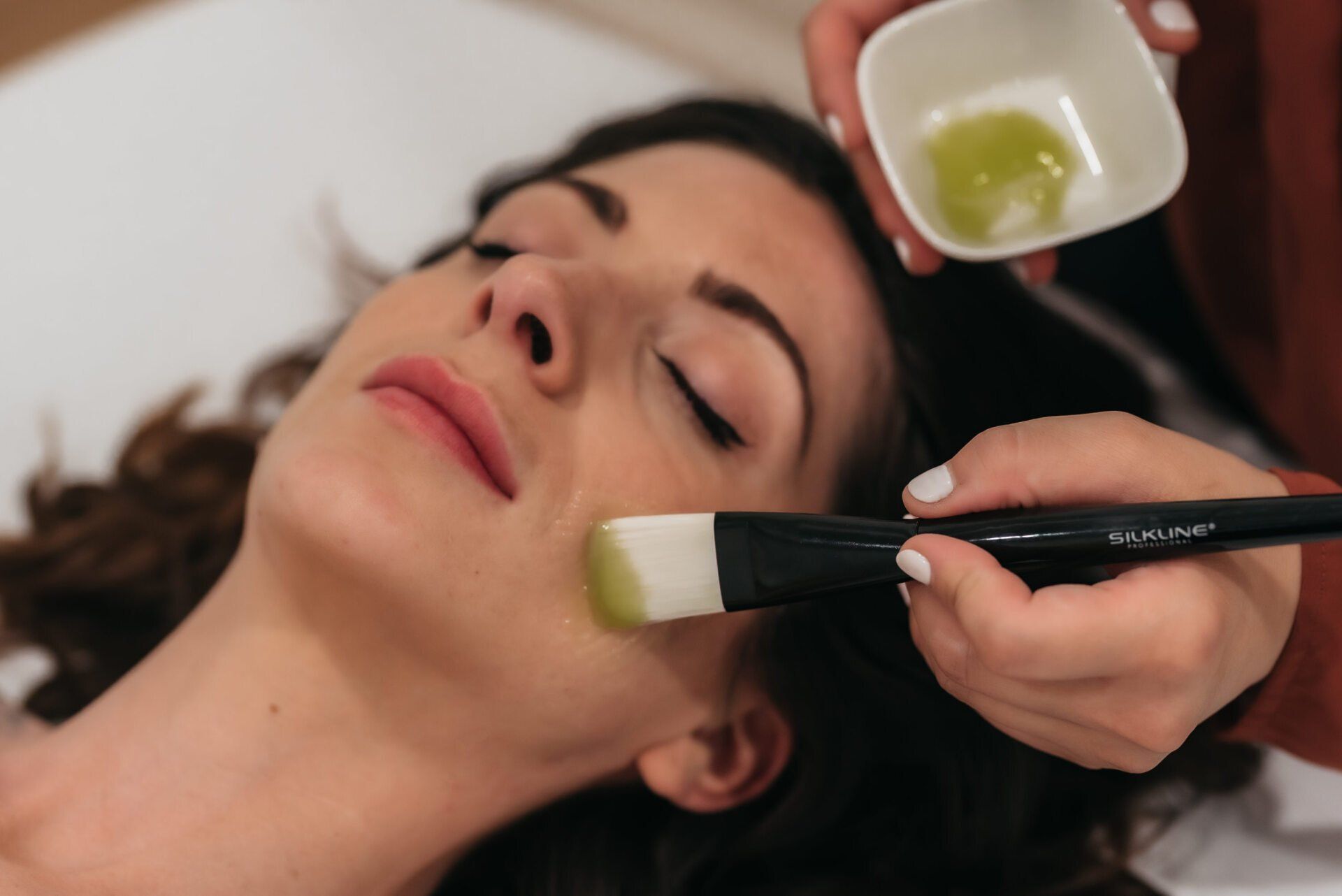 Spa technician applying a facial treatment to a woman lying on a therapy table