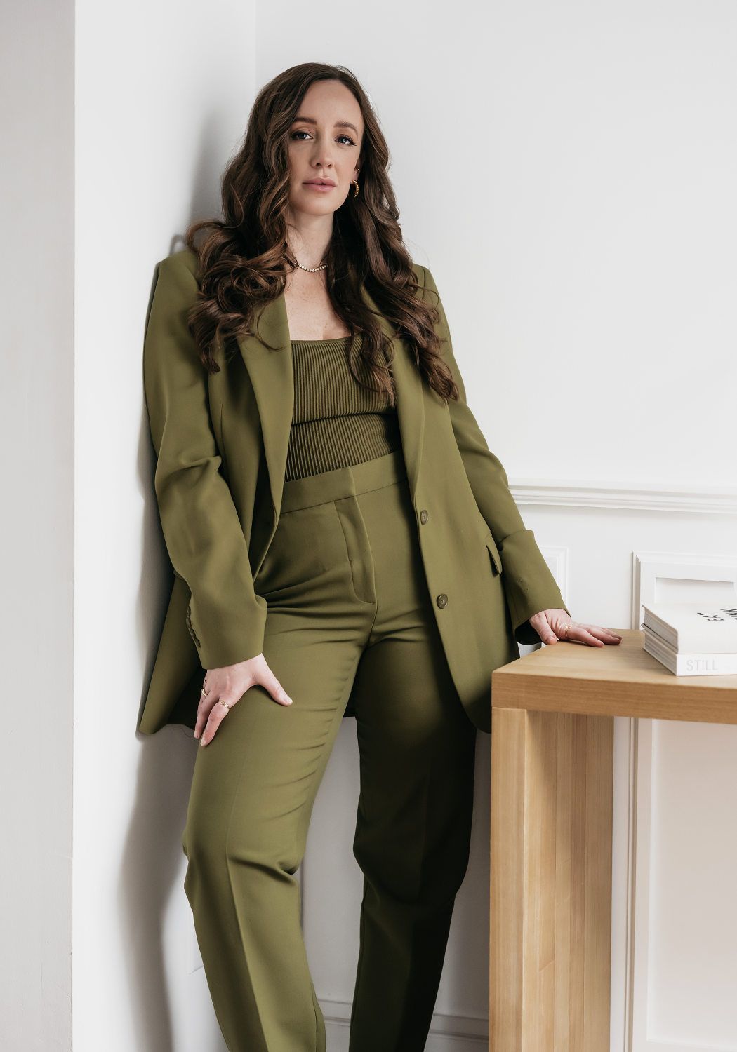 Woman dressed in green, standing confidently against a wall with a relaxed hand resting on her thigh