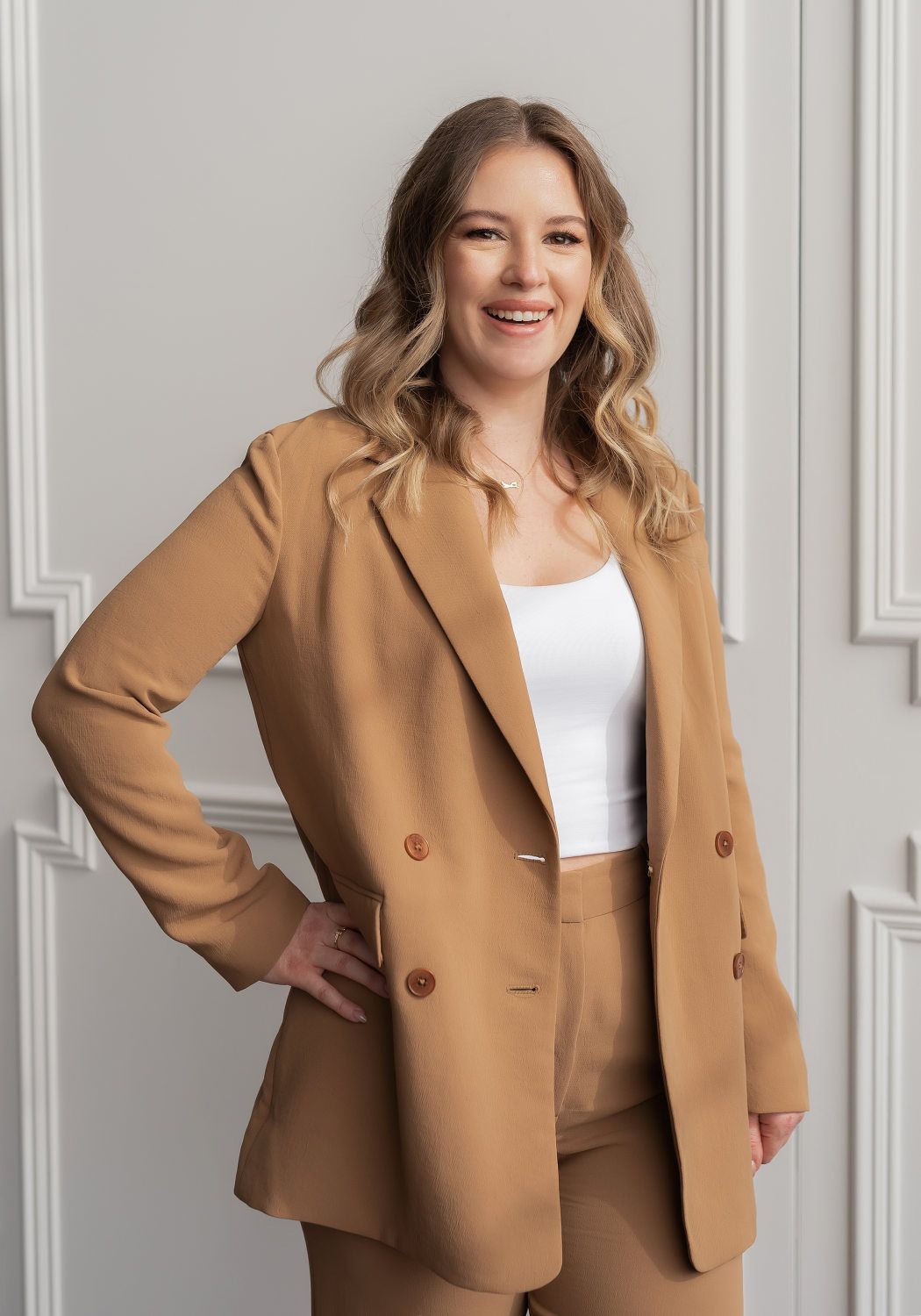 A woman in a tan suit and white top stands confidently, showcasing a professional and stylish appearance.