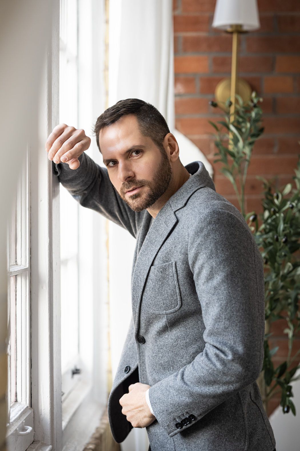 A man in a gray suit posing for headshots by a window in Toronto.