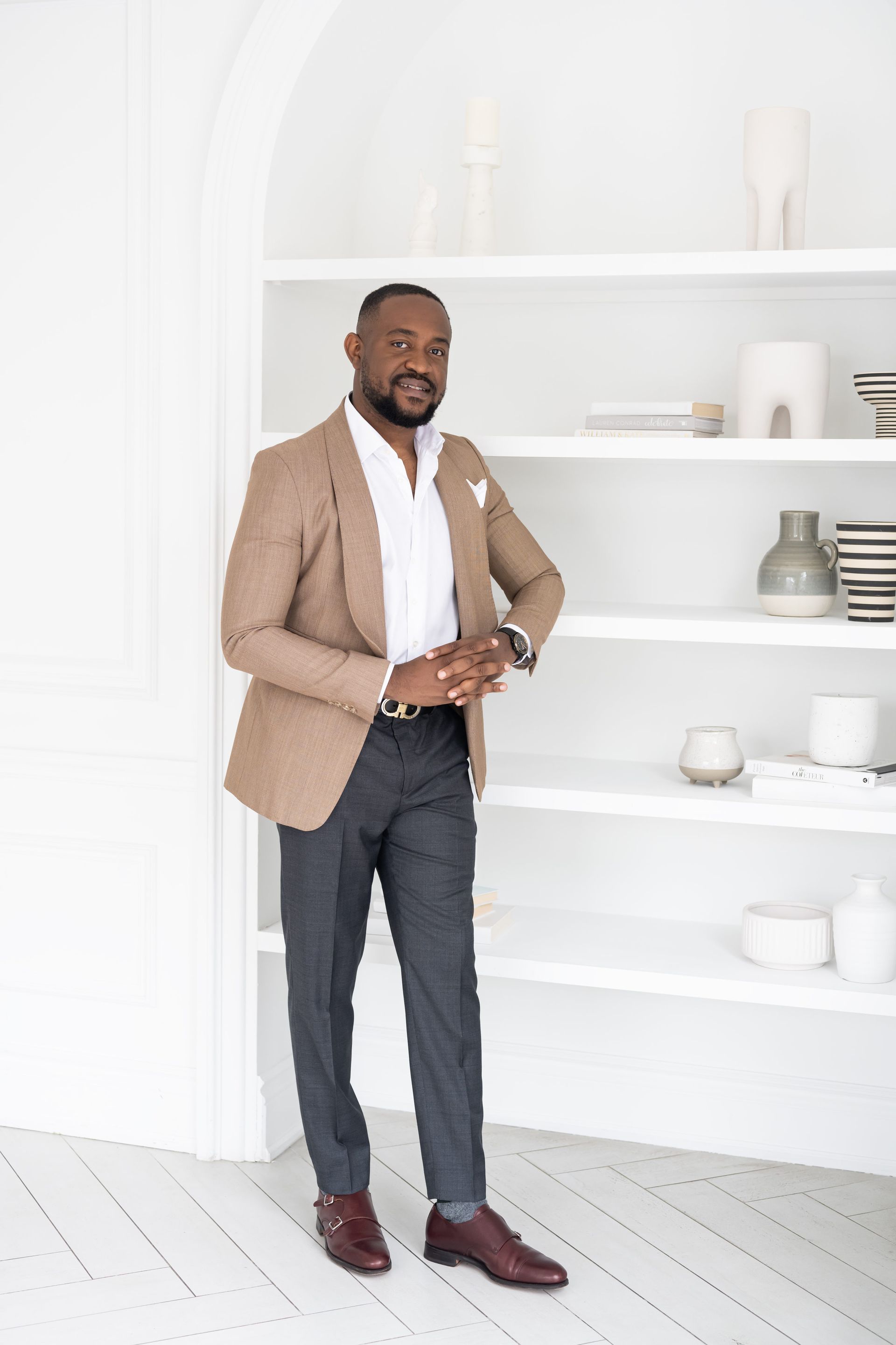 A man in a tan suit posing for professional business headshots in front of shelves.