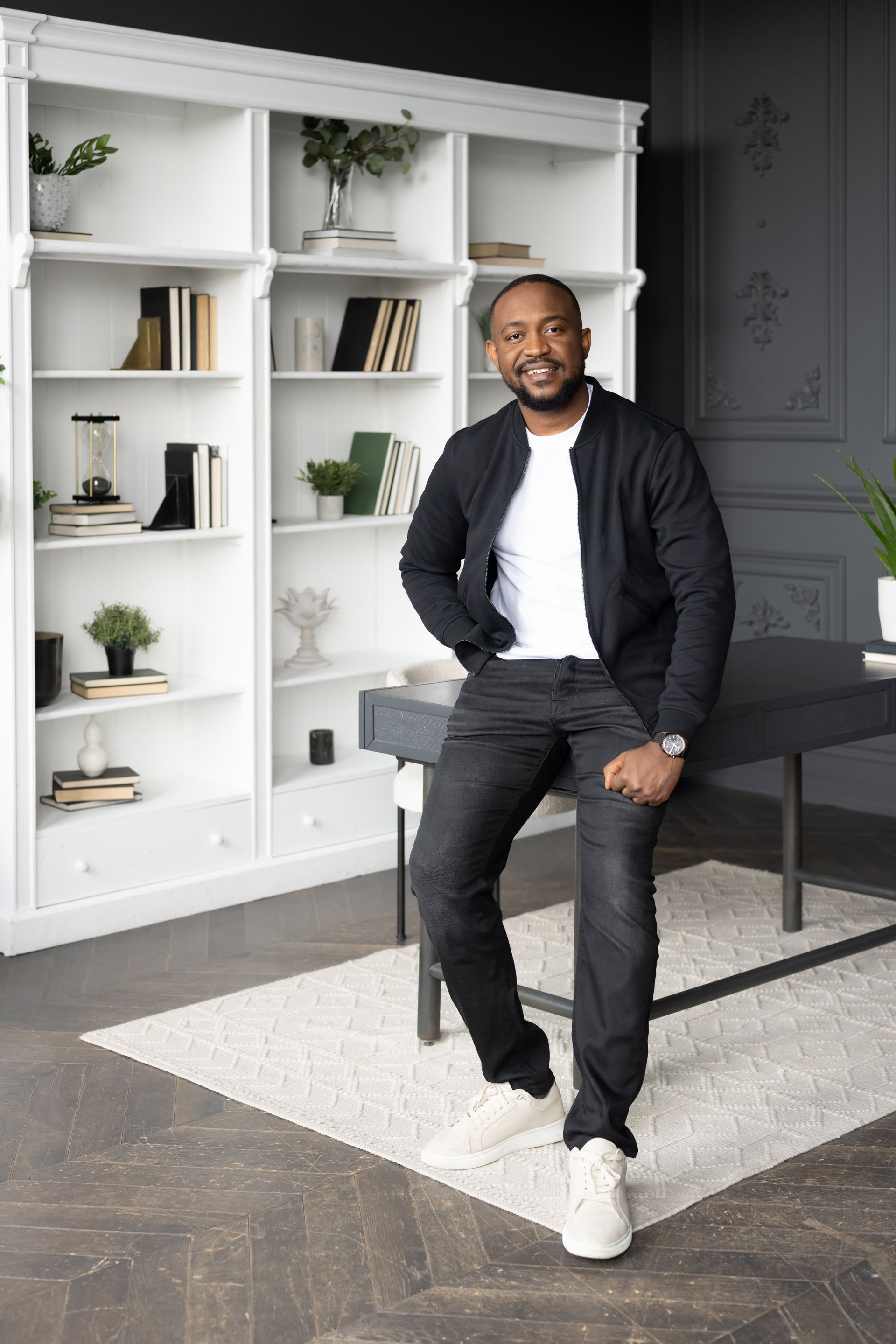 A man posing on a chair for a personal branding photoshoot in front of a bookcase.