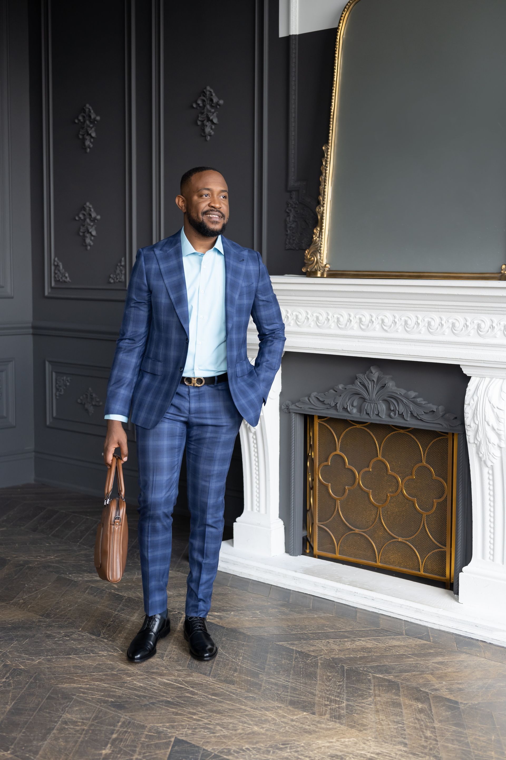 An executive in a suit standing in front of a fireplace.
