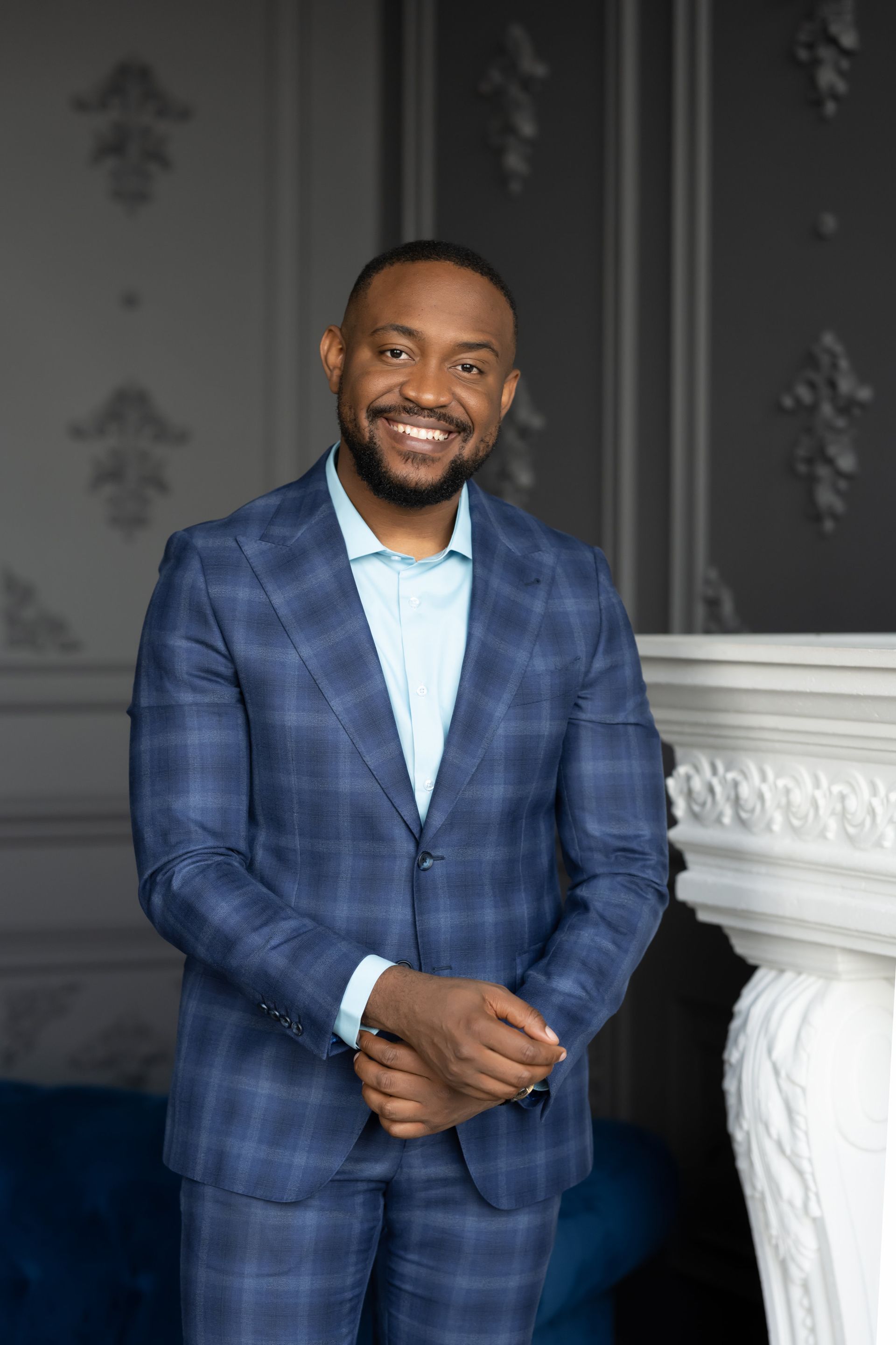 A smiling executive in a blue suit standing in front of a fireplace.