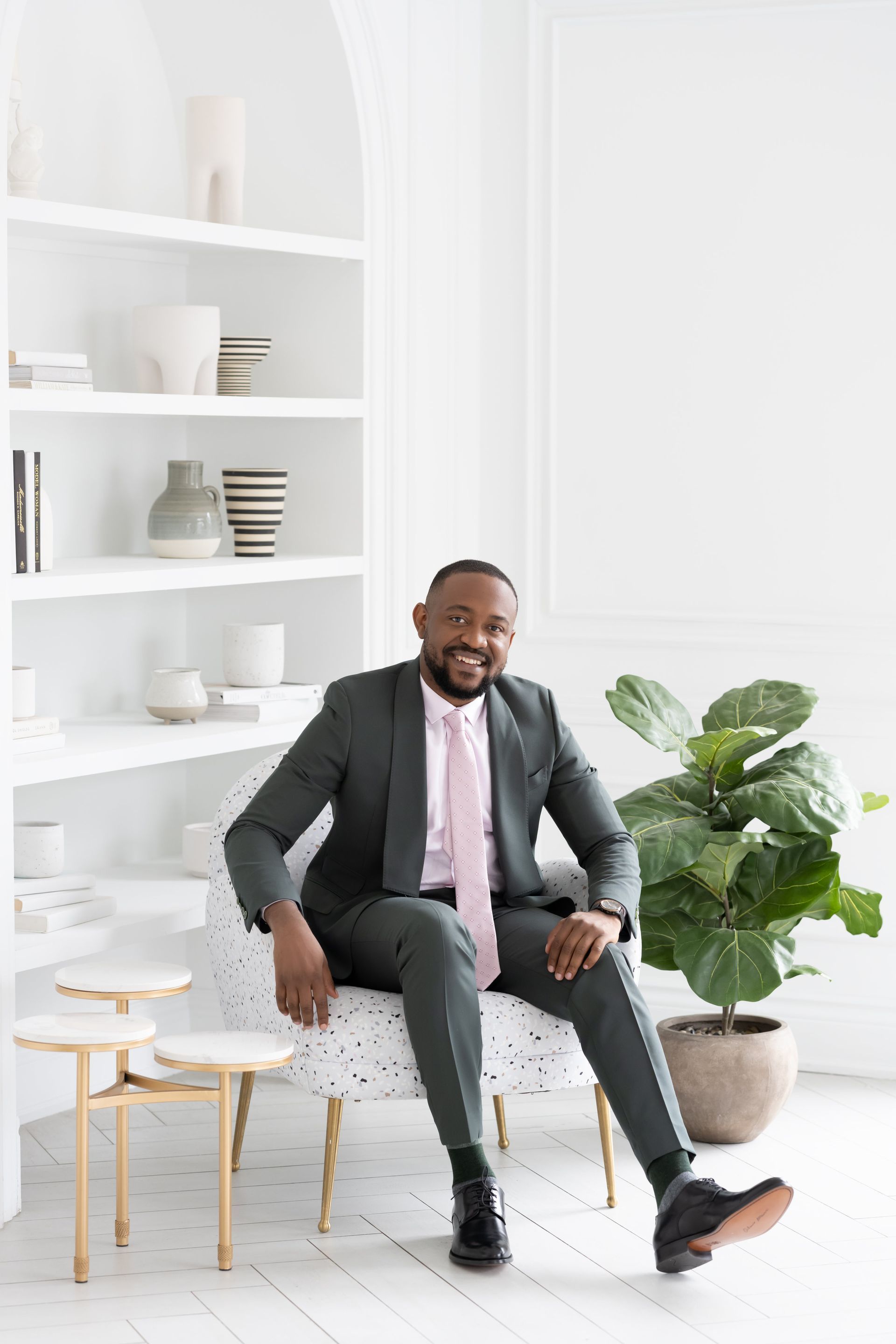 A man in a suit posing on a chair for a branding photoshoot in a white room.
