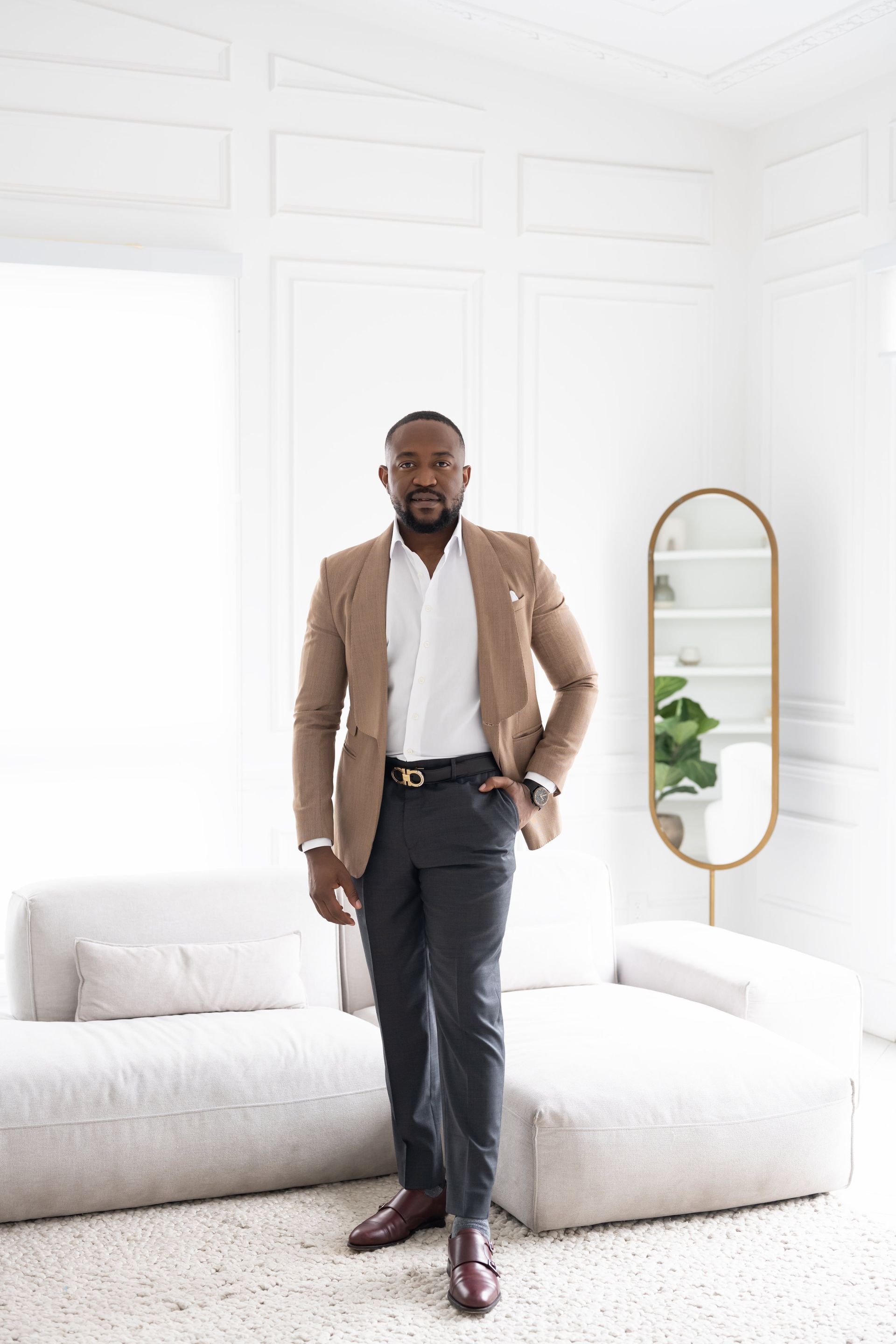 An entrepreneur in a tan blazer standing in front of a white couch.