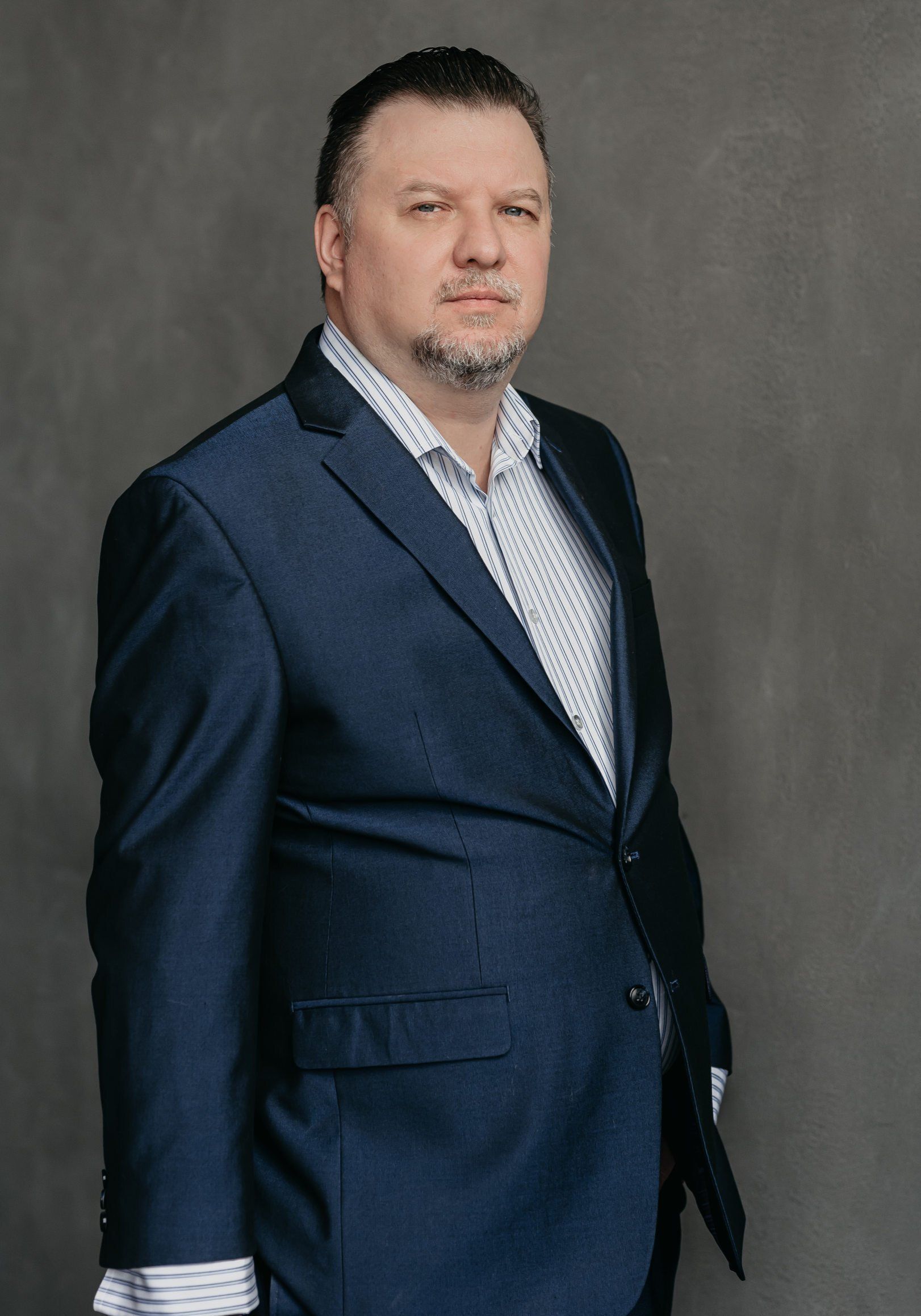 a middle-aged man wearing stripe polo and a black coat looking at the camera