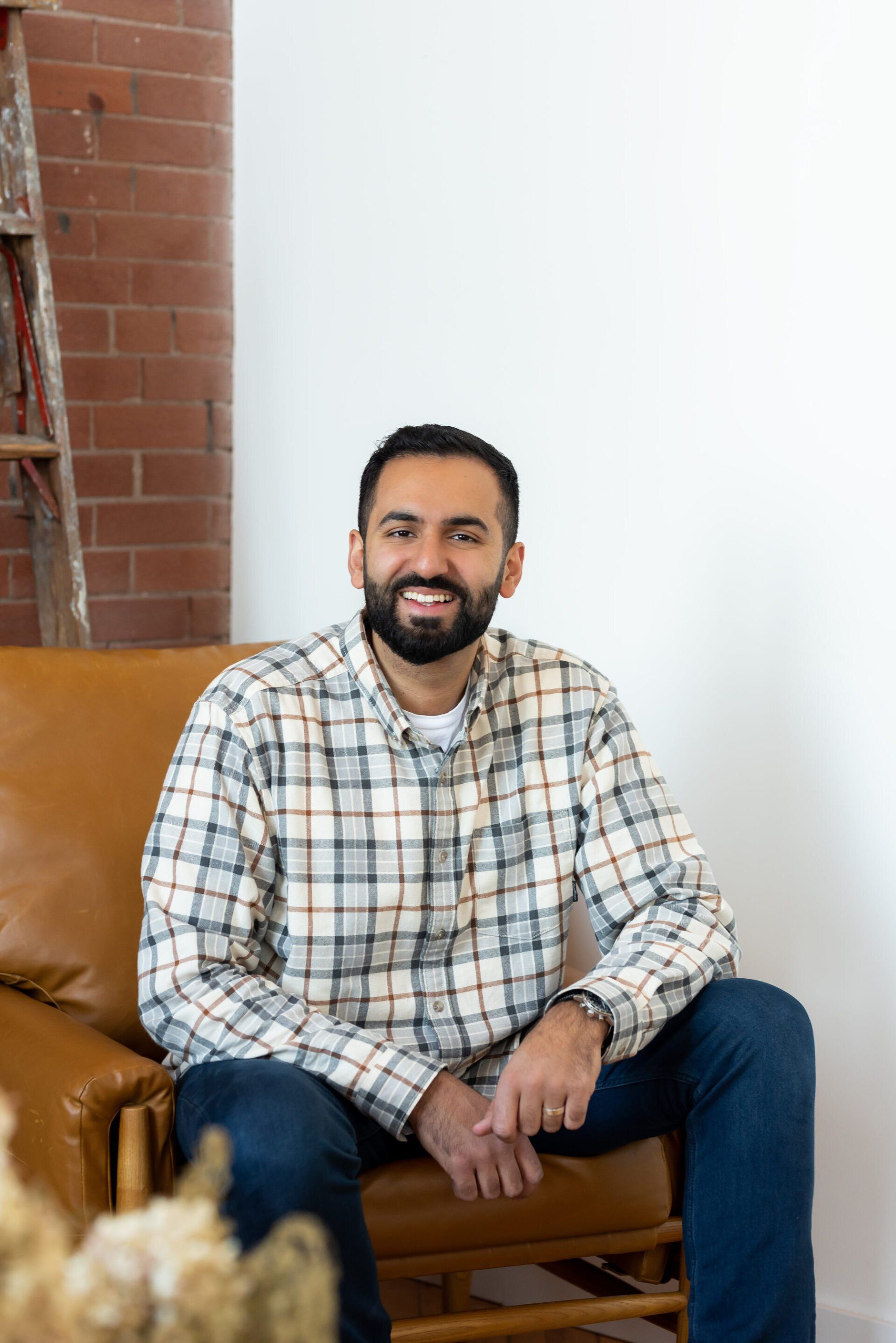 a man with a checkered polo sitting a brown leather couch